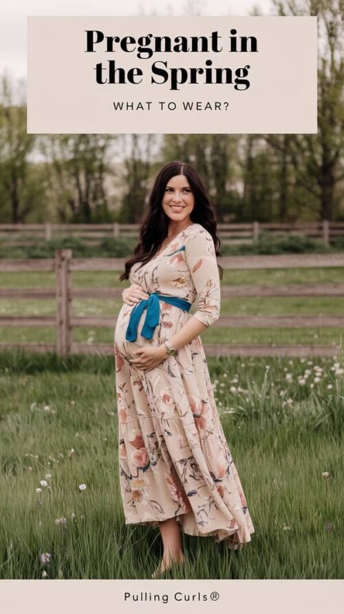 A pinterest pin with a beautiful pregnant woman in the spring wearing a beautiful casual dress. The woman has long dark hair and is wearing a beige dress with floral patterns and a blue belt. She is standing on a green field with wildflowers. The background contains a wooden fence and trees. The top of the pin contains the title "Pregnant in the SPRING" and the subtitle "What to wear?". The bottom of the pin contains the site name "Pulling Curls®".